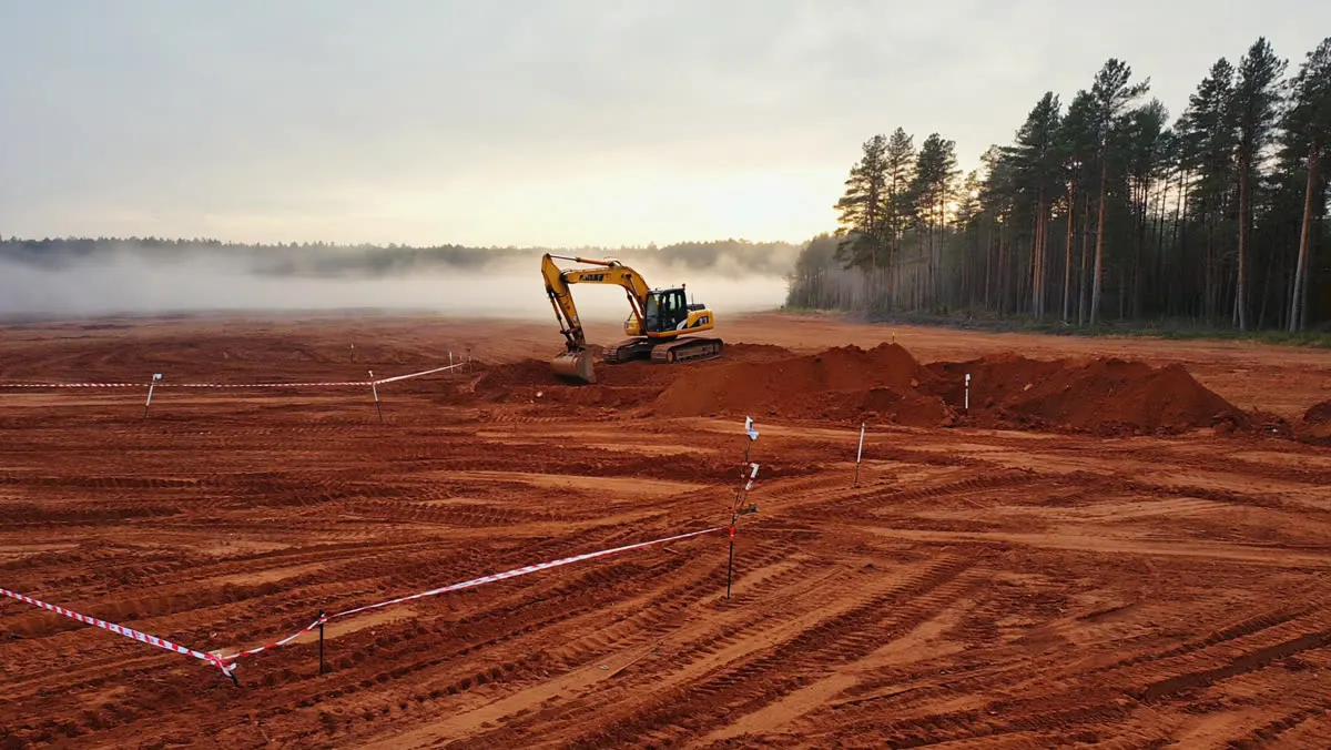 An excavator shaping a building pad on red clay at dawn